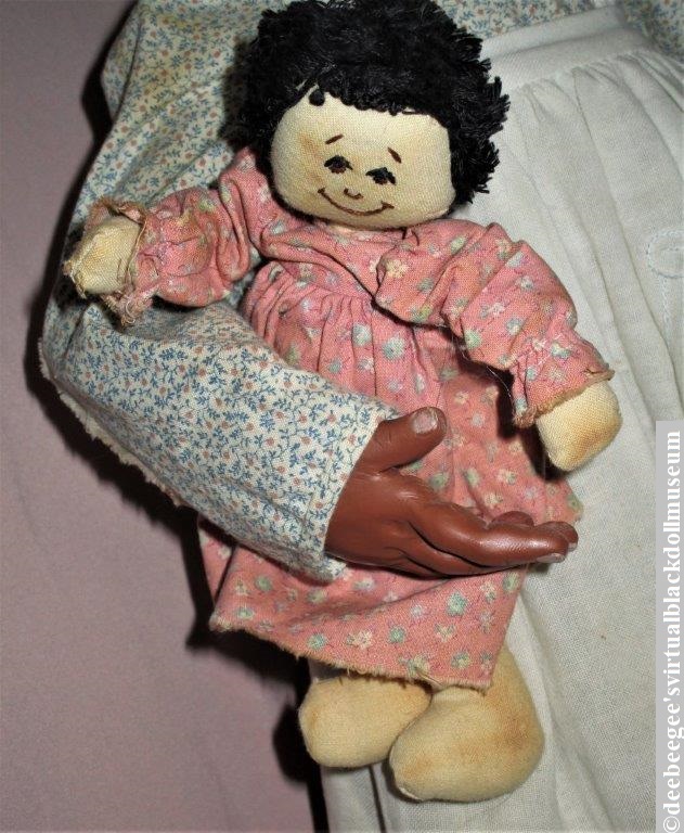 Small white cloth doll held by a larger Black polymer clay doll
